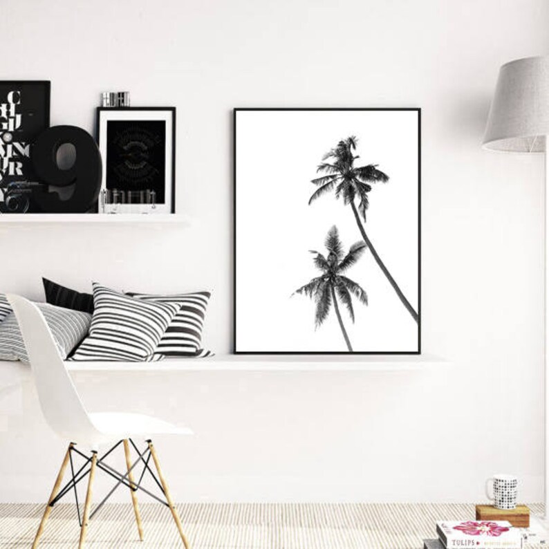 May include: Black and white framed print featuring two palm trees against a white background. The artwork is displayed on a white shelf with decorative items, including pillows, a chair, and other framed art.