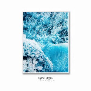 May include: An aerial photograph of a blue ocean with white foamy waves crashing. The water is a deep blue color and the waves are white and foamy. The photo is taken from a high angle, giving a view of the ocean from above.
