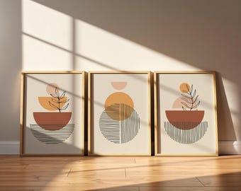 Op de afbeelding: Een set van drie ingelijste wandposters met abstracte geometrische vormen, waaronder cirkels, halve cirkels en lijnpatronen in tinten terracotta, perzik en zwart op een lichtbeige achtergrond, gevat in lichtgekleurde houten lijsten.