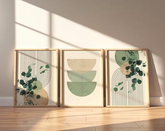 Op de afbeelding: Drie ingelijste wandkunstprints met geometrische ontwerpen en botanische elementen. De buitenste prints tonen zwarte lijn-bogen en groene eucalyptusbladeren, terwijl de middelste print drie gestapelde halve cirkels in beige en groen toont.