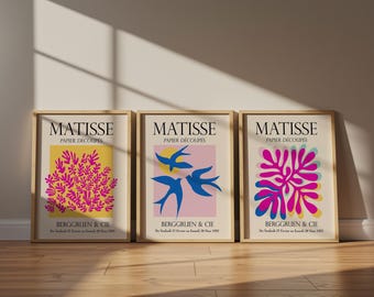 Op de afbeelding: Drie ingelijste kunstprints met Matisse Papier Découpés ontwerpen. De linker print toont magenta organische vormen op een gele achtergrond. De middelste print toont blauwe vogels op een roze achtergrond. De rechter print toont magenta en blauwe bladvormen.