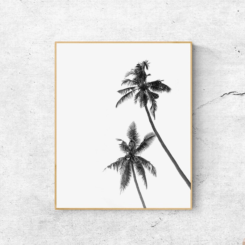 May include: Black and white framed print featuring two palm trees against a bright white background. The palm trees are detailed with visible fronds and trunks, creating a tropical aesthetic. The frame is a light brown color.
