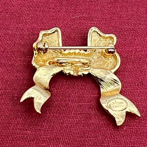 Op de afbeelding: Gouden strik broche met een textuur en een enkele strass in het midden. De achterkant van de broche heeft de woorden "Avon Jewelry" gegraveerd.