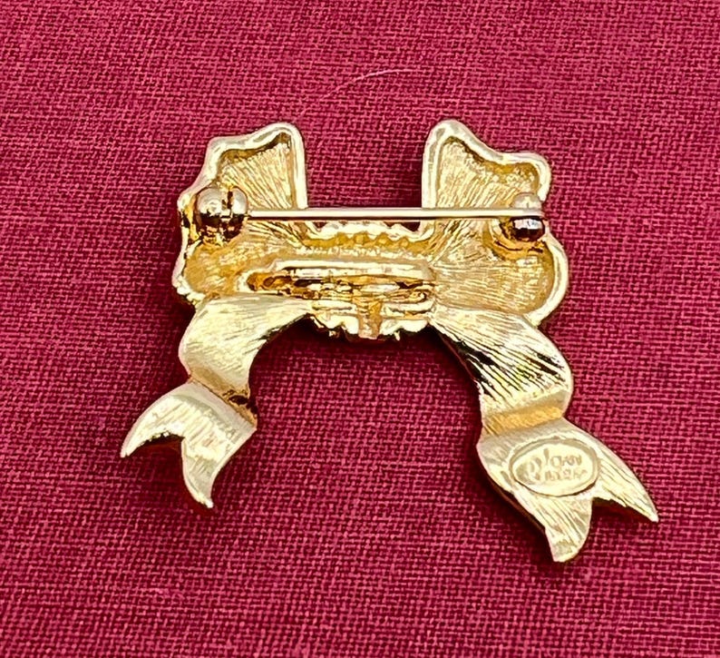 Op de afbeelding: Gouden strik broche met een textuur en een enkele strass in het midden. De achterkant van de broche heeft de woorden "Avon Jewelry" gegraveerd.