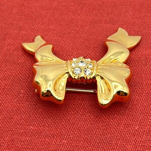 Op de afbeelding: Een gouden strik broche met een helder strass steentje in het midden.