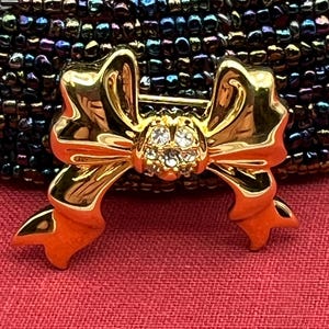 Op de afbeelding: Een gouden strik broche met een cluster van heldere strass steentjes in het midden.