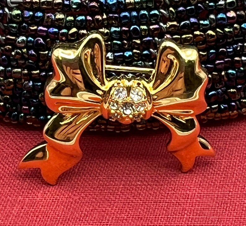 Op de afbeelding: Een gouden strik broche met een cluster van heldere strass steentjes in het midden.