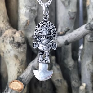 Puede incluir: Collar con colgante de plata que representa una figura estilizada detallada con un tocado y una base en forma de hoja.