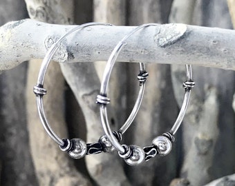 May include: A pair of silver hoop earrings with three small beads on each hoop.