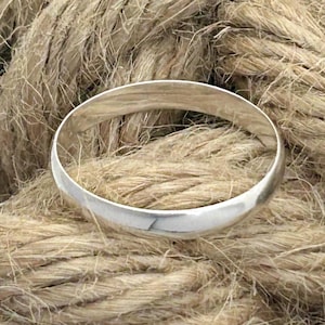Op de afbeelding: Een gepolijste zilverkleurige ring met een glad, afgerond buitenoppervlak. De ring heeft een eenvoudig, doorlopend cirkelvormig ontwerp met een reflecterende metalen afwerking die het licht opvangt en een strak en uniform uiterlijk toont.