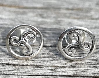 May include: A pair of silver stud earrings featuring a Celtic knot design. The earrings are circular and have a three-dimensional design.