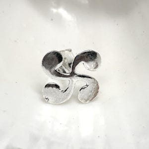 May include: Silver earring with a stylized swirl design.