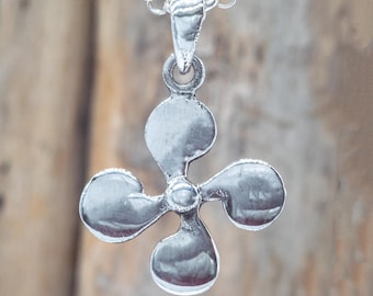 Op de afbeelding: Zilverkleurige ketting met een hanger in de vorm van een Baskisch kruis met vier lobben. De hanger hangt aan een fijne ketting. De hanger heeft een getextureerd oppervlak. De achtergrond is wazig, waardoor de focus op de ketting ligt.