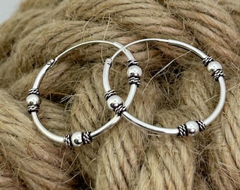 May include: A pair of silver hoop earrings featuring a smooth circular band accented with three evenly spaced polished silver beads, each flanked by small decorative twisted wire rings that provide a textured contrast to the metal surface.