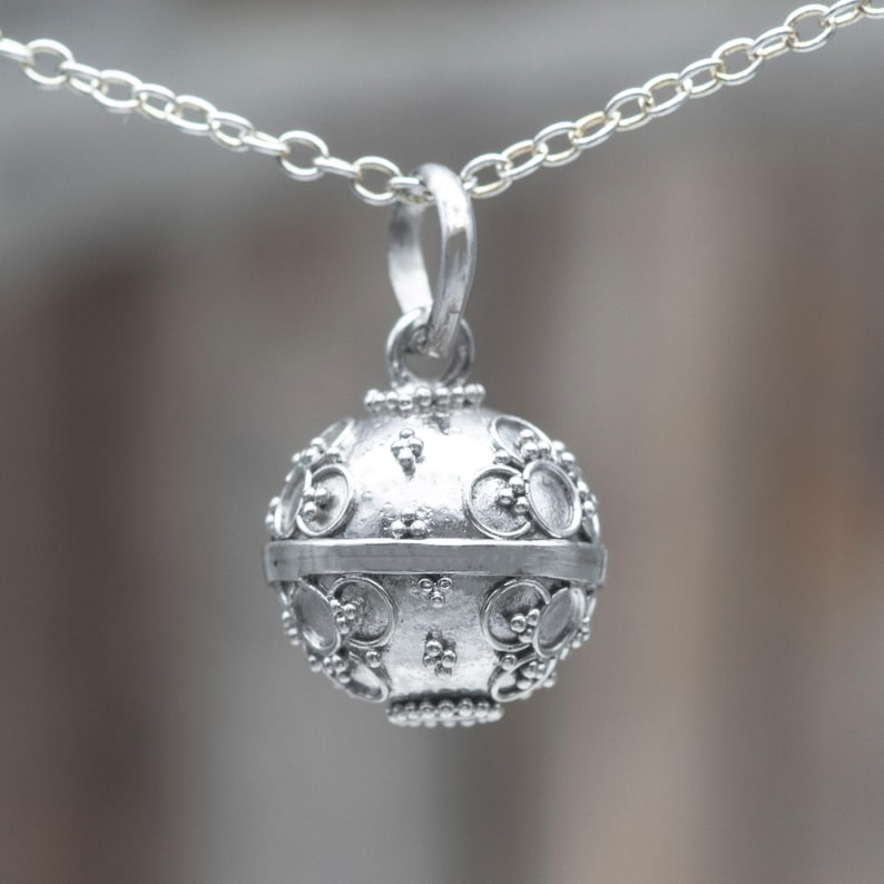 May include: A silver necklace with a round, ornate pendant. The pendant has a textured surface with a repeating pattern of circles and dots.