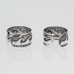 Könnte beinhalten: Zwei silberfarbene, verstellbare Ringe mit einem strukturierten Wellendesign. Die Ringe haben ein offenes Design und werden auf einer reflektierenden Oberfläche präsentiert. Die Ringe sind wahrscheinlich aus Metall und für verschiedene Fingergrößen geeignet.