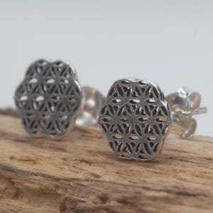 Può includere: Un paio di orecchini a lobo in argento. Ogni orecchino presenta un design a fiore della vita con intricati motivi traforati. Gli orecchini sono esposti su un pezzo di legno su sfondo bianco.