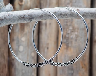May include: A pair of silver hoop earrings with a decorative design on the front. The hoops are thick and have a smooth finish.