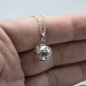 May include: A silver necklace with a detailed, round pendant. The pendant has a textured surface and appears to be a charm or a locket.