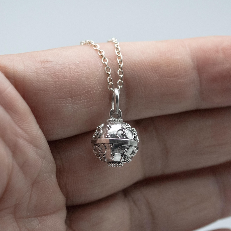 May include: A silver necklace with a detailed, round pendant. The pendant has a textured surface and appears to be a charm or a locket.