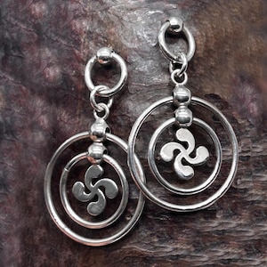 May include: A pair of silver earrings with a circular design. Each earring features a small silver ball, a larger circle, and a smaller circle with a four-leaf clover design inside.
