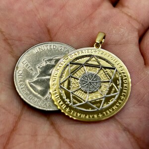 May include: Gold-toned pendant with intricate geometric designs and inscribed text. The pendant is circular, with a central star pattern and surrounding text. A U.S. quarter is next to the pendant for size comparison.