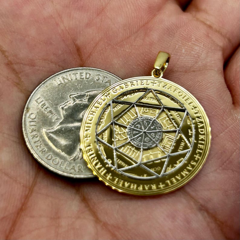 May include: Gold-toned pendant with intricate geometric designs and inscribed text. The pendant is circular, with a central star pattern and surrounding text. A U.S. quarter is next to the pendant for size comparison.