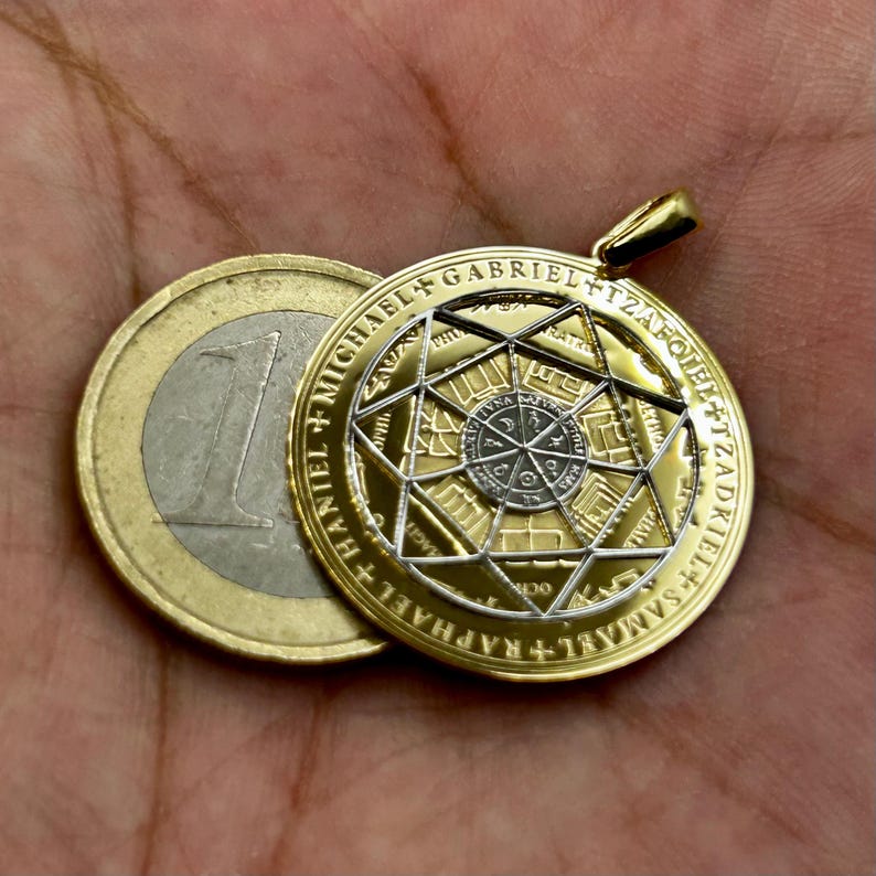 May include: A gold-colored pendant with a detailed geometric design, featuring a central star and inscribed text. The pendant is round and has a bail for a chain. A Euro coin is next to the pendant for size comparison.