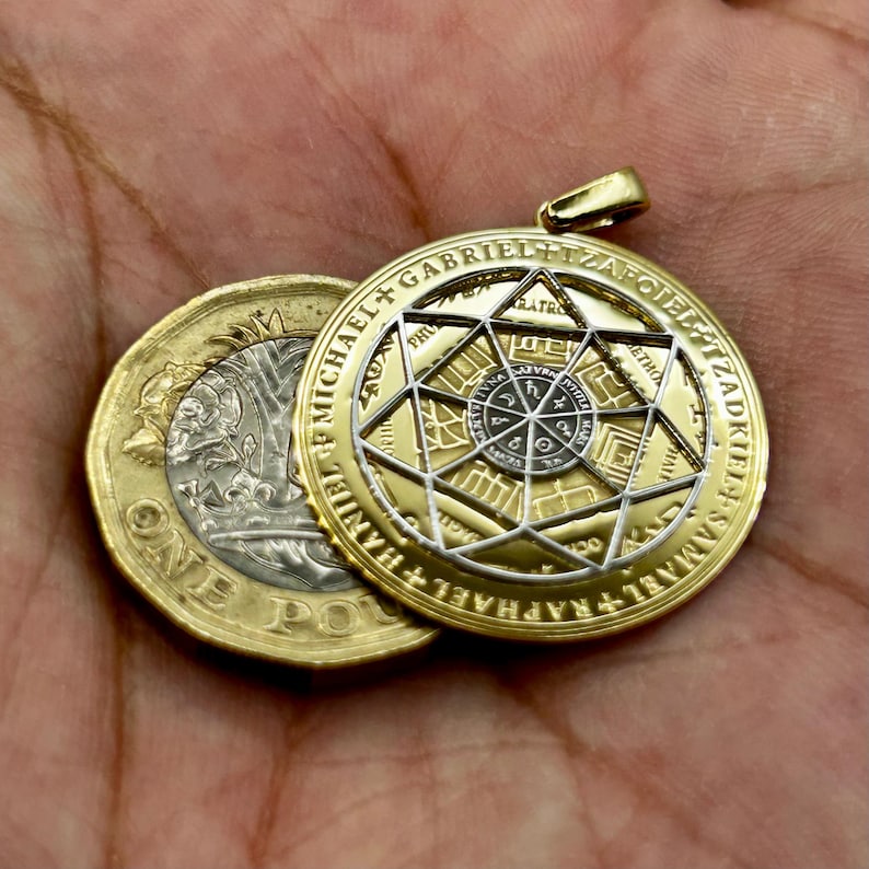 May include: A gold-colored pendant with a complex geometric design and the names of archangels inscribed around the edge. The pendant is next to a British one-pound coin. The pendant has a gold bail.