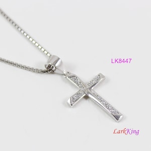 May include: A silver chain necklace with a silver cross pendant. The cross is decorated with small, clear stones.