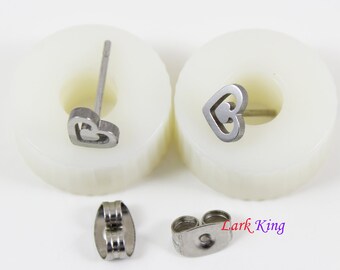 May include: A pair of silver heart-shaped stud earrings with a matching pair of silver earring backs. Lark King is printed on the white surface.