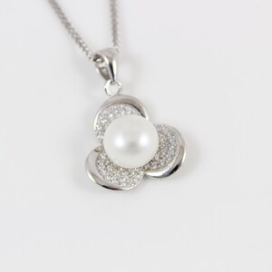 Puede incluir: Un collar de plata con un colgante de flor de perla y cristal.