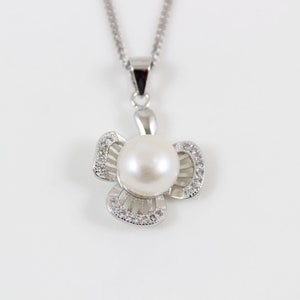 Puede incluir: Un collar de plata con un colgante en forma de flor que presenta una perla blanca en el centro y piedras de circonita cúbica transparentes alrededor de los bordes.