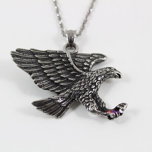 May include: Silver toned eagle pendant necklace. The eagle is in flight with its wings spread and talons extended. The necklace has a silver chain.