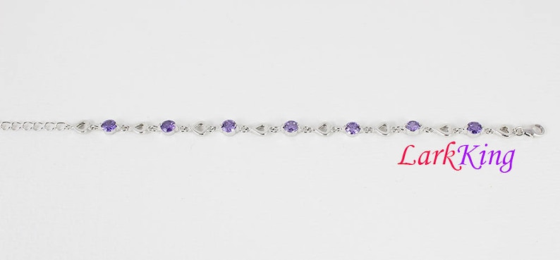 May include: A silver bracelet with a delicate chain and purple gemstones. The bracelet features a heart-shaped design.