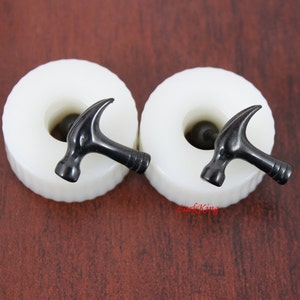 May include: A pair of black hammer-shaped earrings on white display stands. The earrings are made of metal and have a shiny finish.