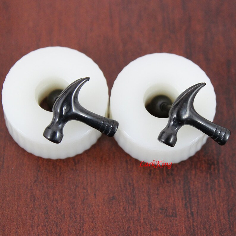 May include: A pair of black hammer-shaped earrings on white display stands. The earrings are made of metal and have a shiny finish.