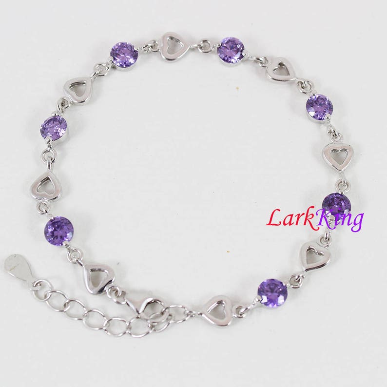 May include: A silver bracelet with a heart-shaped design and purple gemstones. The bracelet has a lobster clasp closure.