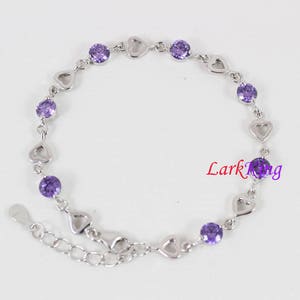 May include: A silver bracelet with a heart-shaped design and purple gemstones. The bracelet has a lobster clasp closure.