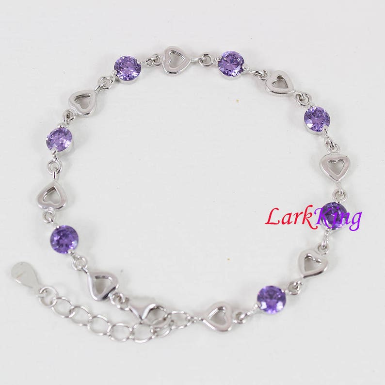 May include: A silver bracelet with a heart-shaped design and purple gemstones. The bracelet has a lobster clasp closure.