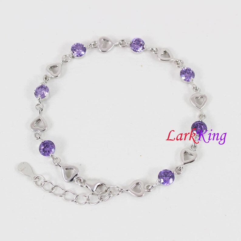 May include: A silver bracelet with a heart-shaped design and purple gemstones. The bracelet has a lobster clasp closure.