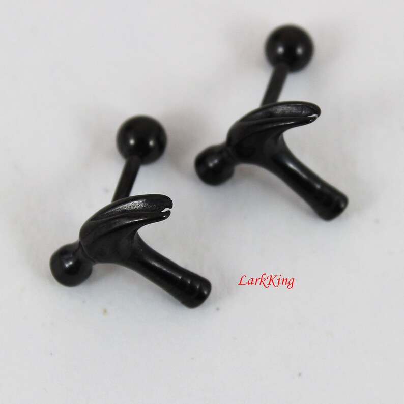 May include: A pair of black hammer-shaped barbell earrings. The earrings have a small black ball on each end.