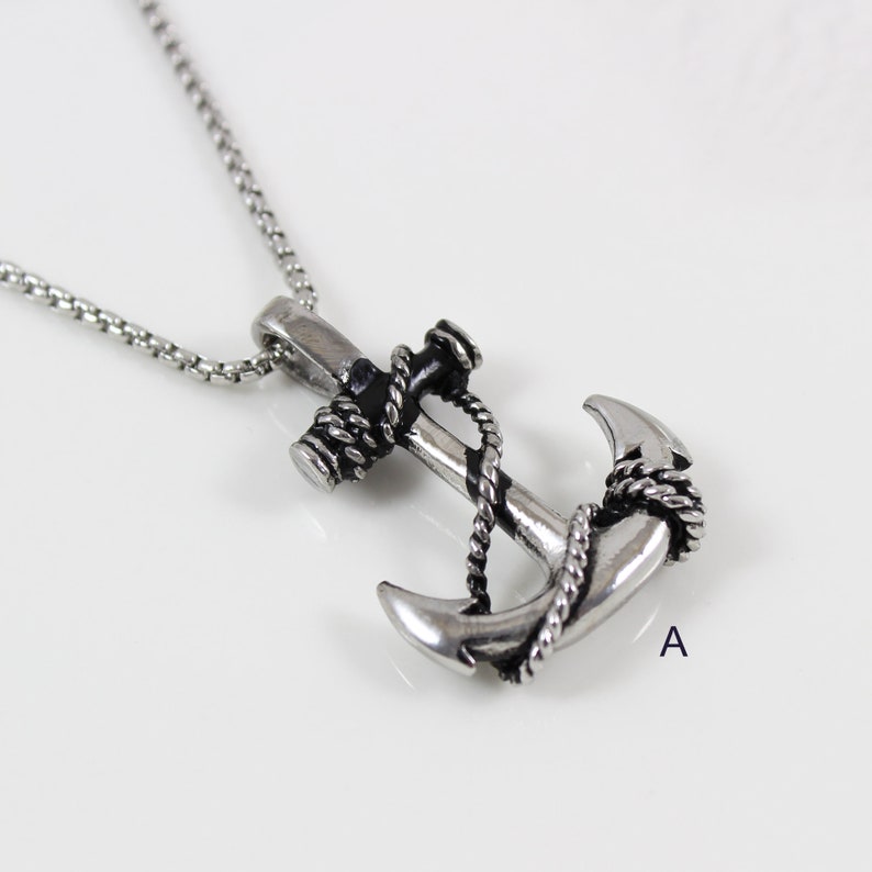 May include: A silver anchor necklace with a black rope detail. The anchor is a detailed design with a black rope wrapped around it.