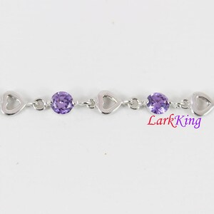 May include: A silver bracelet with a heart-shaped design and purple gemstones. Lark King is printed on the bracelet.