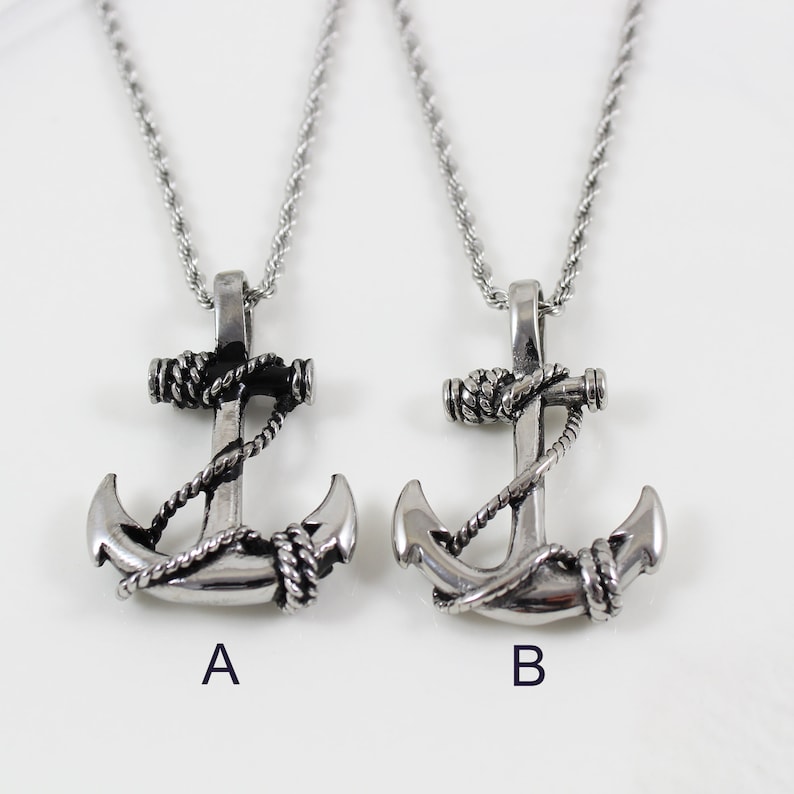 May include: Two silver anchor necklaces with black rope detail. The anchors are identical except for the rope detail, which is slightly different on each necklace. The necklaces are on a white background.