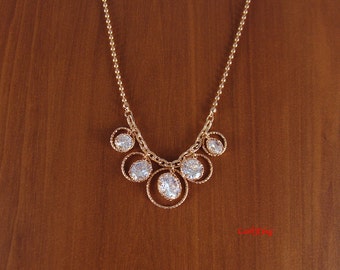 May include: A gold necklace with a delicate chain and a pendant featuring five clear round stones set in gold circles.