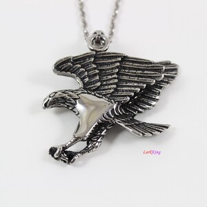May include: Silver toned stainless steel eagle pendant necklace. The eagle is in flight with its wings spread wide. The pendant is detailed with intricate feather markings.