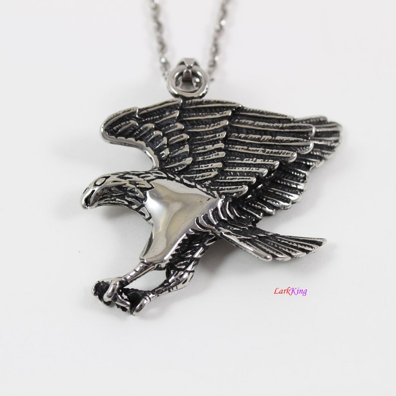 May include: Silver toned stainless steel eagle pendant necklace. The eagle is in flight with its wings spread wide. The pendant is detailed with intricate feather markings.