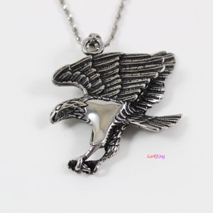 May include: Silver toned pendant necklace featuring a detailed eagle design with spread wings. The eagle is in flight with its talons extended.
