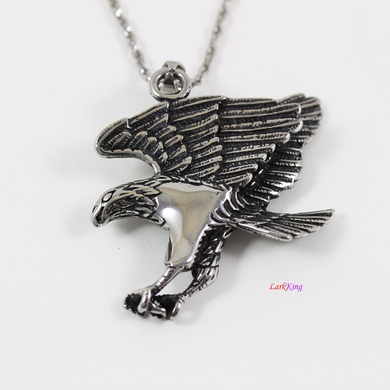 May include: Silver toned pendant necklace featuring a detailed eagle design with spread wings. The eagle is in flight with its talons extended.